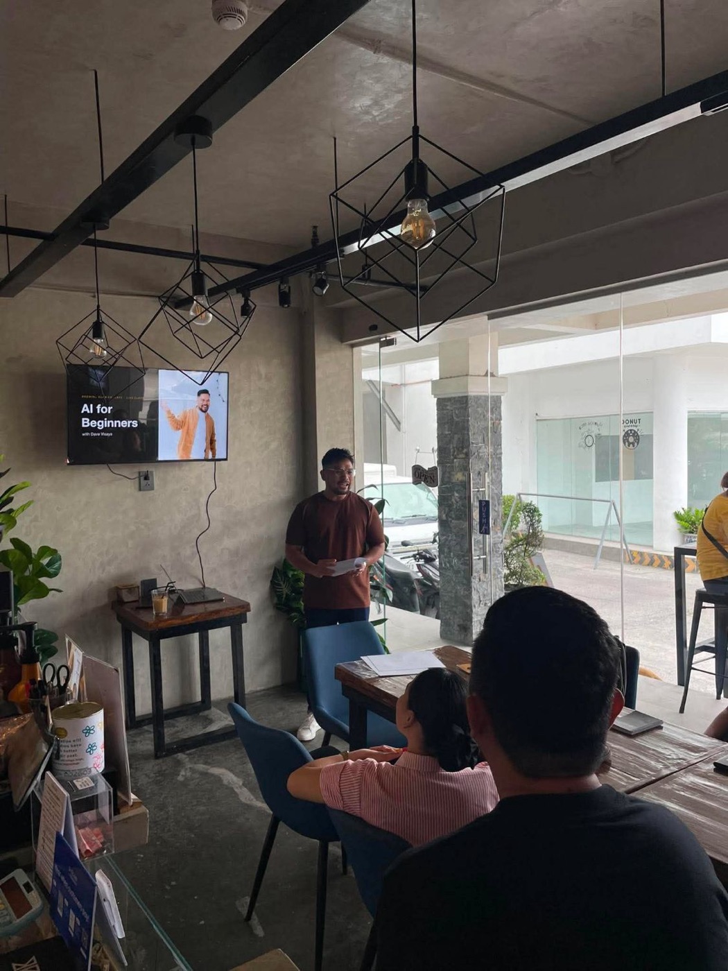Dave Visaya teaching AI for Beginners at Brewing Club Co. Cafe, his title slide on the screen and business owners listening