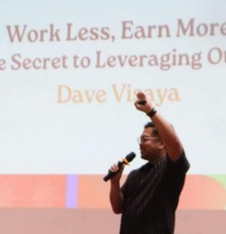 Dave Visaya speaking on stage, with his talk title Work Less, Earn More on the screen behind him